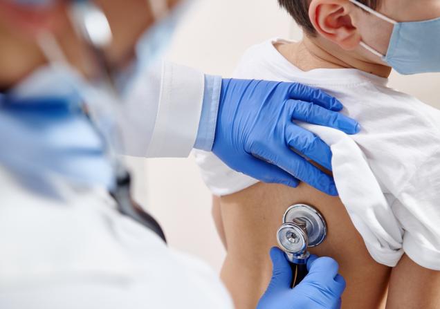 A doctor listens to a child's lungs via a stethoscope. Image by Taras Grebinets via Shutterstock