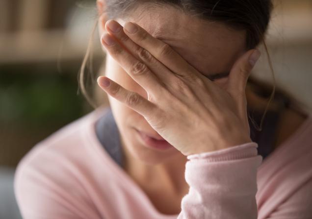 A woman holds her head in her hand. Image by fizkes via Shutterstock