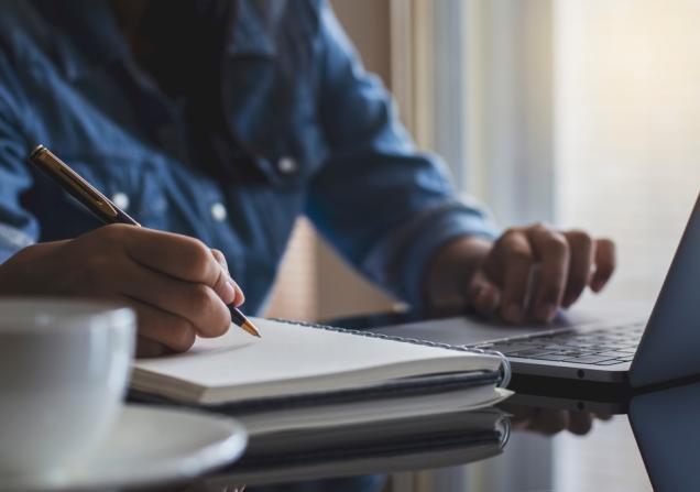 Person taking notes while working on a laptop. Image by NIKCOA via Shutterstock