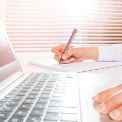 A person using a laptop and taking notes. Image by Sergey Novikov via Shutterstock.